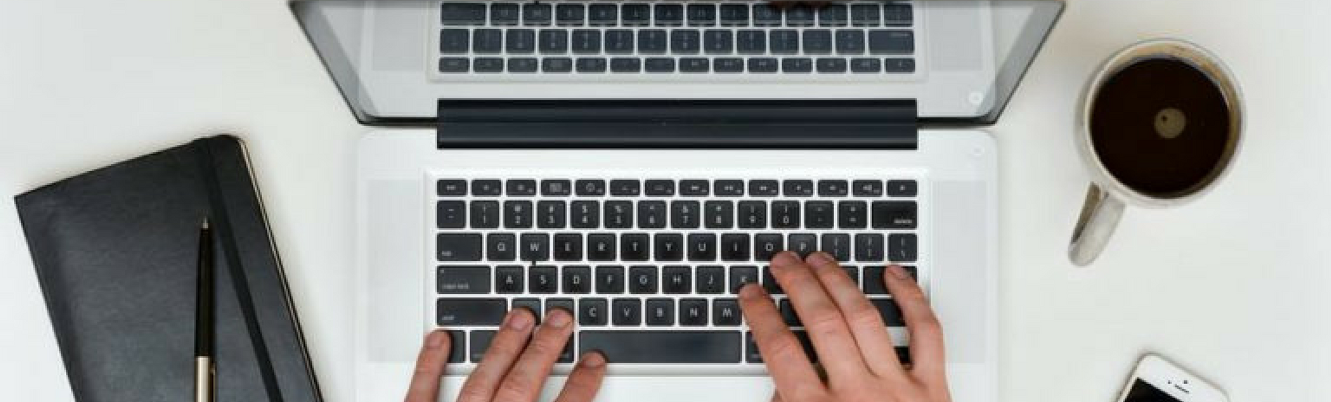Hands typing on laptop with tablet and coffee cup surrounding represent how easy clocking in can be using an online time clock instead of a physical time clock.