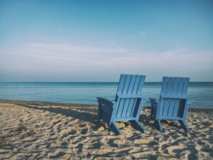 Two beach chairs set on beach overlooking ocean and twilight sky.