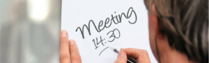 Manager writes meeting time on dry erase board in leading employees in time management.