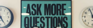 Sign displaying "Ask More Questions" between two time clocks suggests finding out more information about Fingercheck.