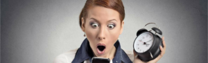 (Surprised) business woman with alarm clock looking at smartphone with Fingercheck alert notifications of punches for employee through email, text message, and punch notification.