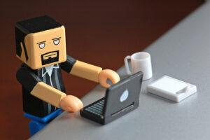 Mini lego figure at desk with laptop typing to demonstrate an employee looking at Fingercheck's table of local overtime laws.