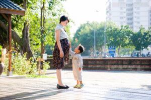 Pregnant woman stands in park with small son touching her belly, symbolizing the transition into motherhood while still holding a job.