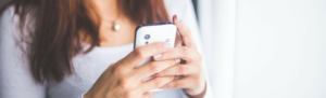 Woman in natural light holding smartphone to view latest updates to the Fingercheck Mobile app.