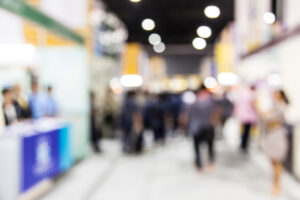 Trade show blurred, busy, signifying the need to prepare for trade show to stand out.