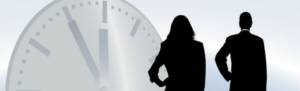 Shadowy figures of businessman businesswoman standing in front of large time clock signifying time worked whether it's part-time or full-time, and the need for staffing solutions.