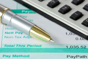 Calculator, payroll reconciliation figures and pen.