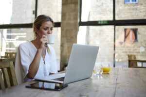 Female employee sits at laptop in beautiful open office making web punch to clock into work.