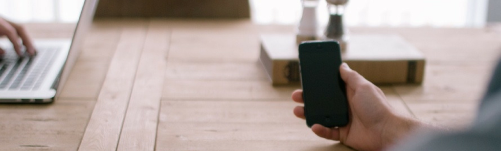 Businessman seated in an open office uses smartphone to manage employees paperlessly.