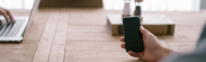 Businessman seated in an open office uses smartphone to manage employees paperlessly.