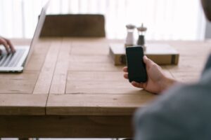 Businessman seated in an open office uses smartphone to manage employees paperlessly.
