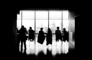 Shadowy figures seated in front of large bright window in council hearing of wage and hour issues.