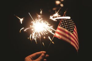 A girl's hand holds a sparkler and the U.S. flag.