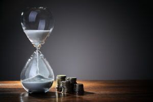 An hourglass of sand tipped over with coin currency stacked next to it, symbolizing the commodity time off is.