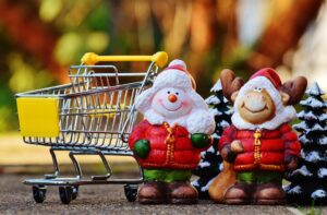 Snowman and reindeer figures stand grinning with mini shopping cart during holiday season