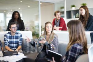 Manager seated in open discussion with employees in bright white office, addressing how time off will be doled out during the holidays using Fingercheck's time and attendance system.