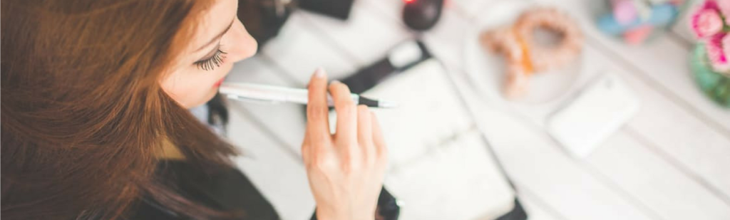 Preoccupied young woman sits at desk holding pen to face, wondering about the limits of time tracking and pondering privacy concerns.