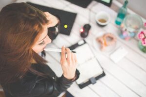 Preoccupied young woman sits at desk holding pen to face, wondering about the limits of time tracking and pondering privacy concerns.