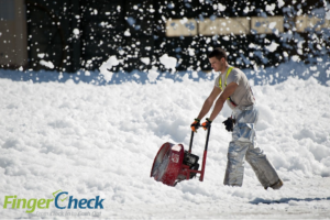 Male employee works clearing snow during winter weather blizzard.