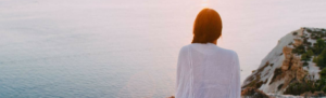 Young woman looks out at ocean as she learns to unplug from work during her summer vacation.