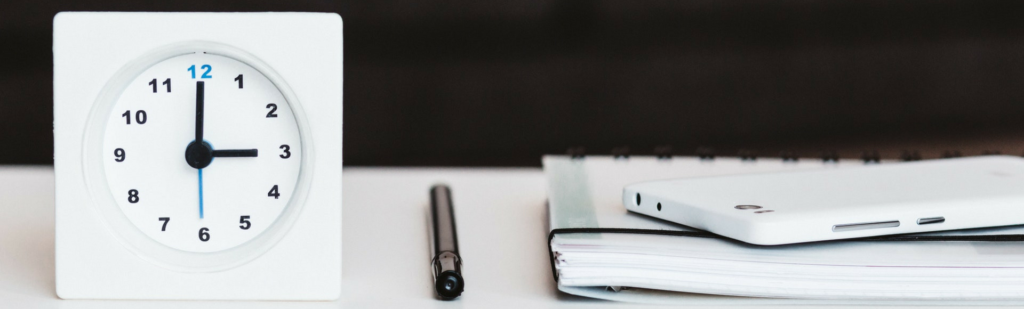 Business environment with time clock displayed next to pen and paper to represent documented time entries to import to Fingercheck.